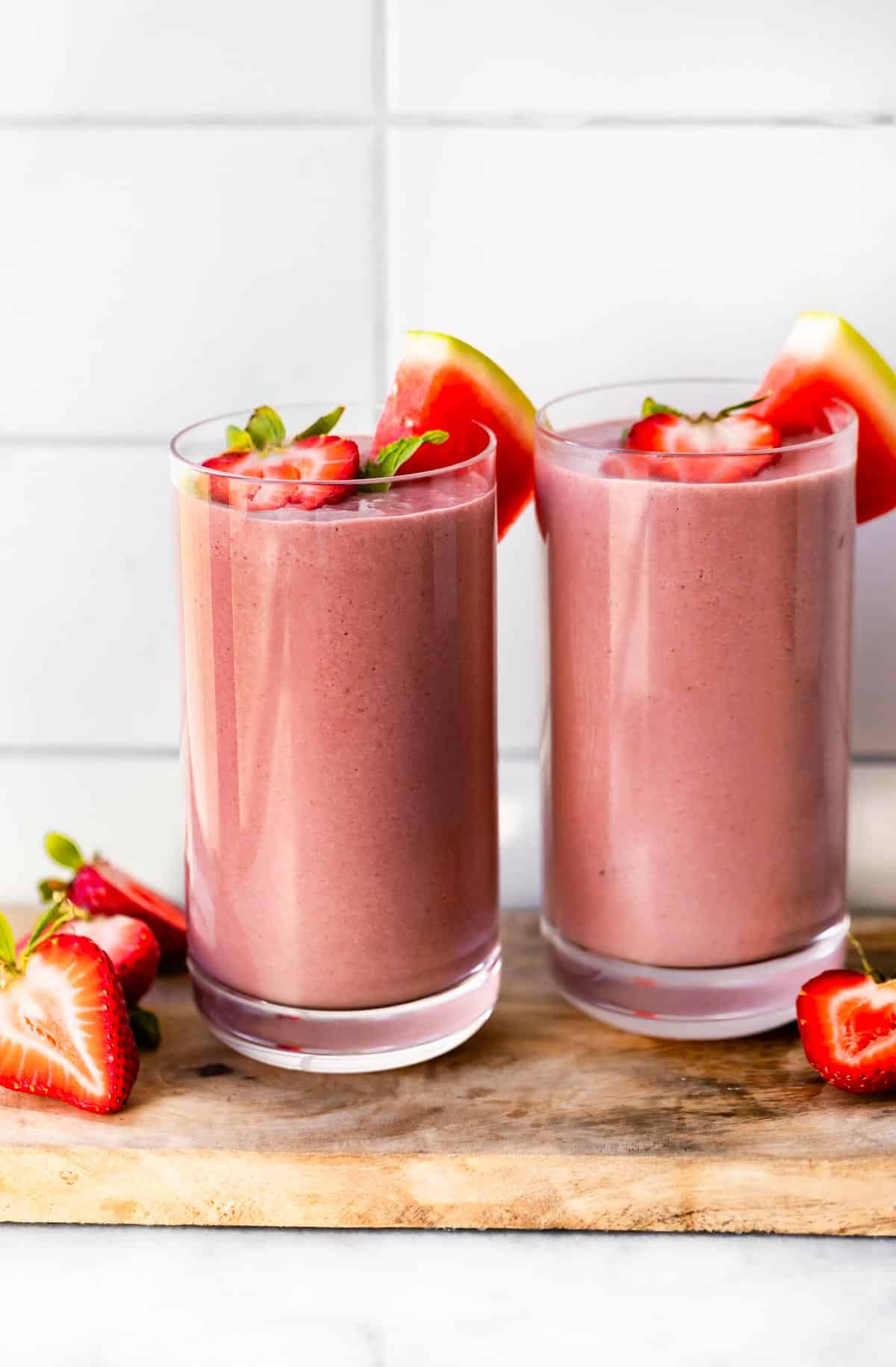 Two glasses of vegan watermelon smoothies topped with halved strawberries and watermelon wedge.