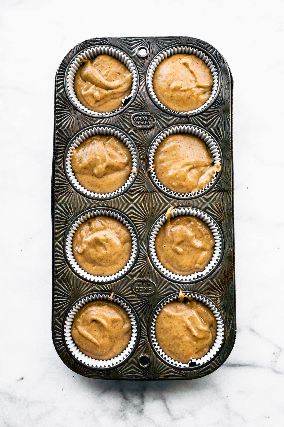 A muffin tin with 8 muffin cups filled with peanut butter banana muffin batter.