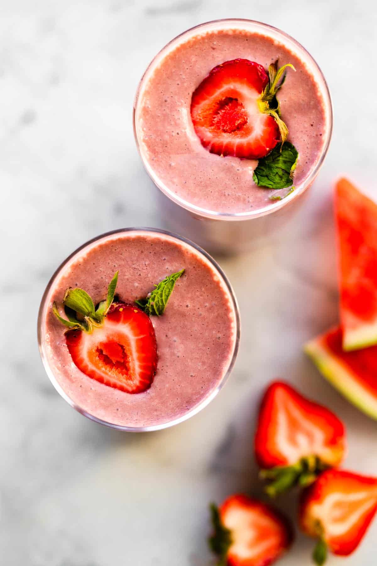 Overhead photo of pretty pink watermelon smoothies topped with halved strawberries.