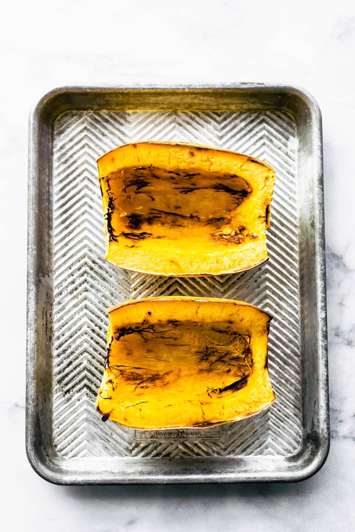 Two halves of baked spaghetti squash on a baking sheet.