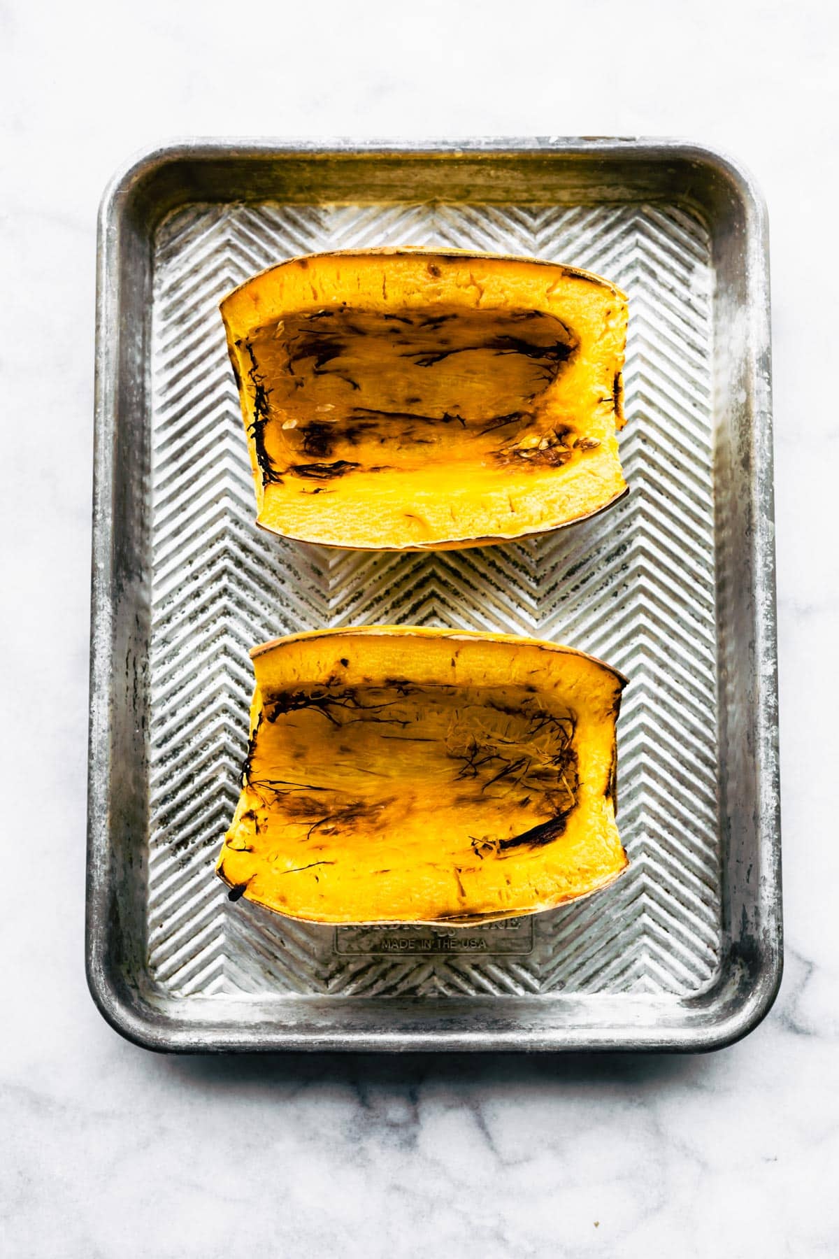 Two halves of baked spaghetti squash on a silver baking sheet