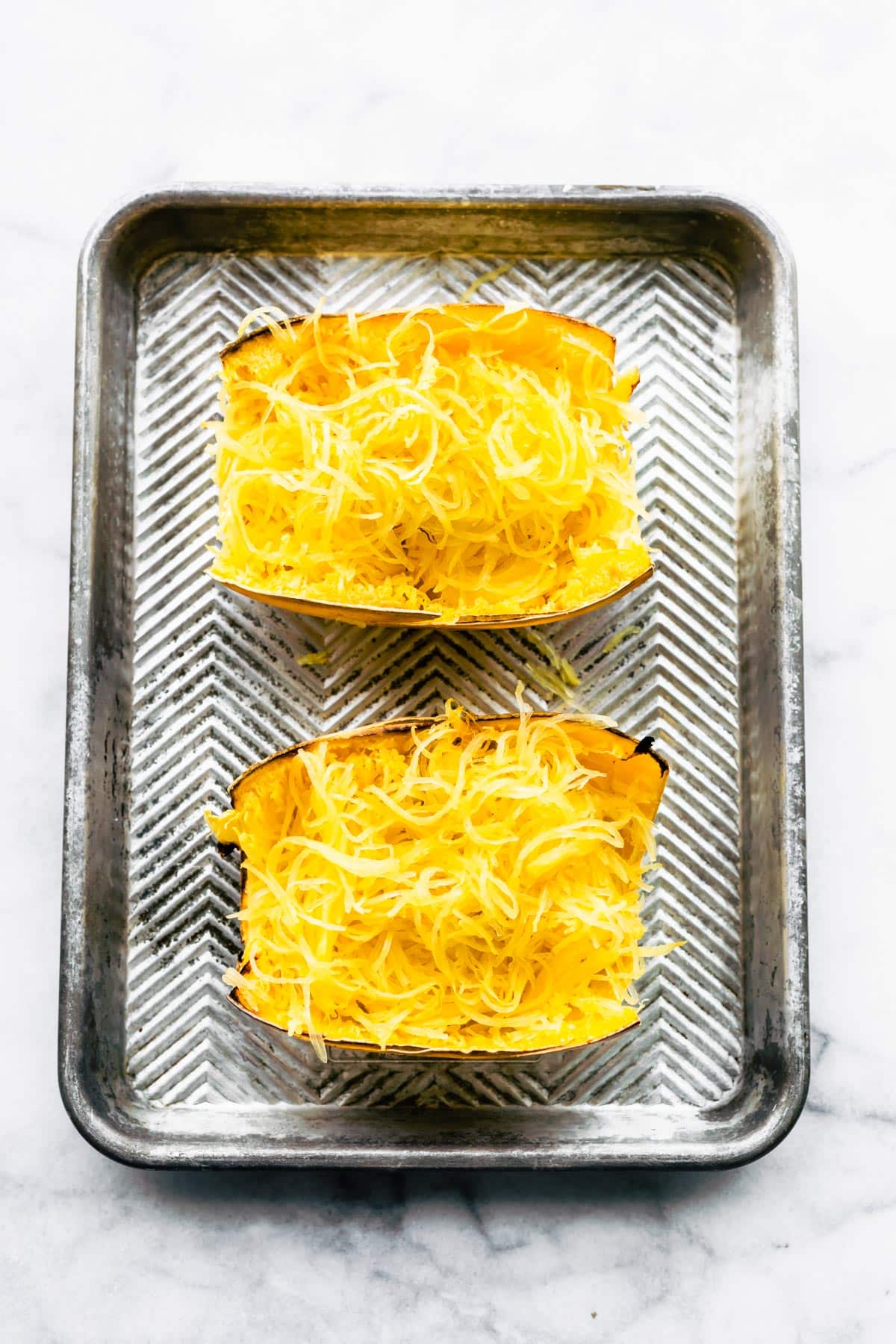 Two spaghetti squash halves filled with spaghetti squash noodles on a baking sheet.