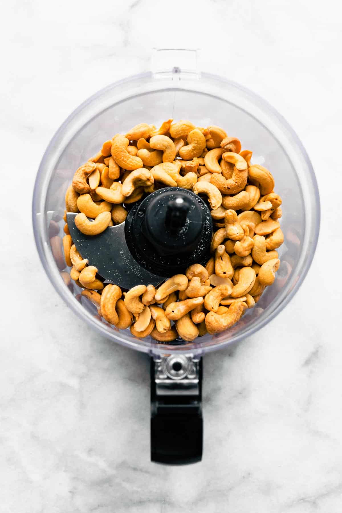 Raw cashews in a food processor ready to be made into vegan cashew butter.