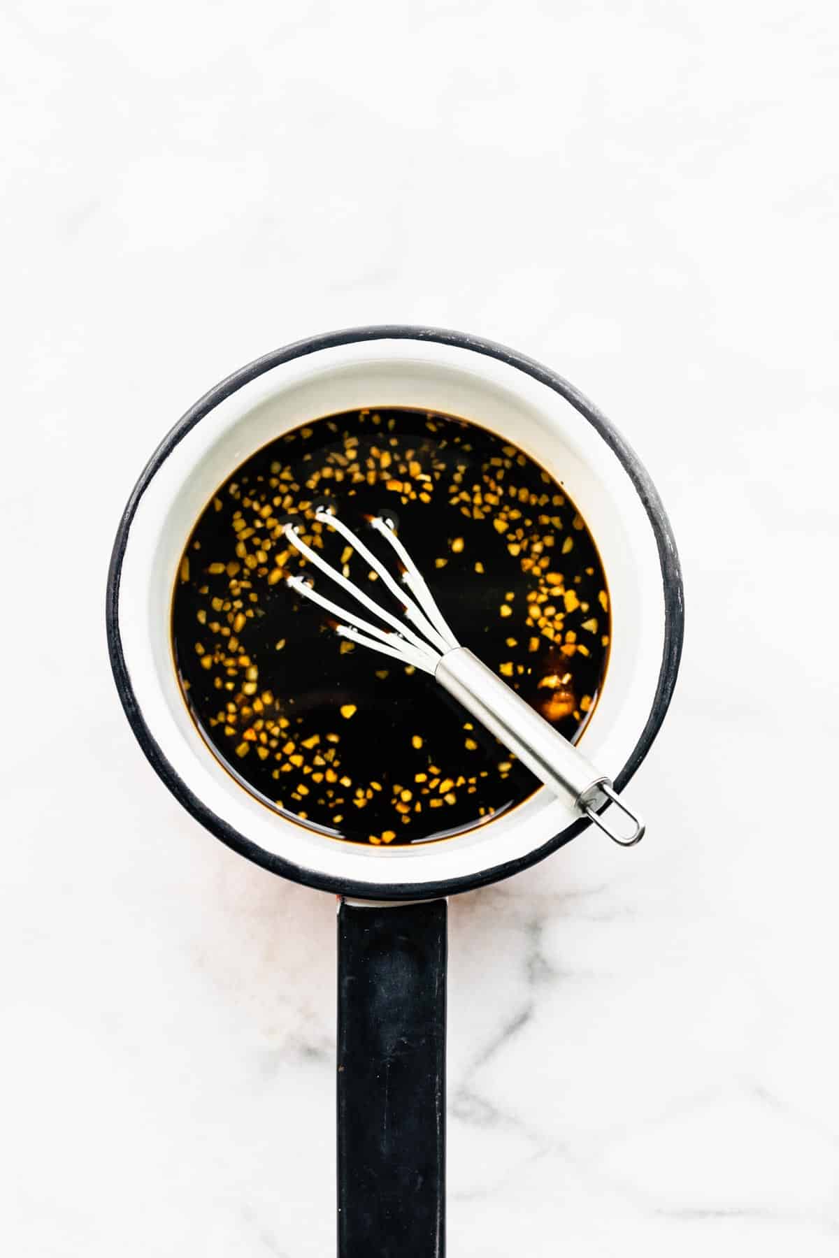 Overhead photo of a whisk stirring homemade teriyaki sauce in a white saucepan.