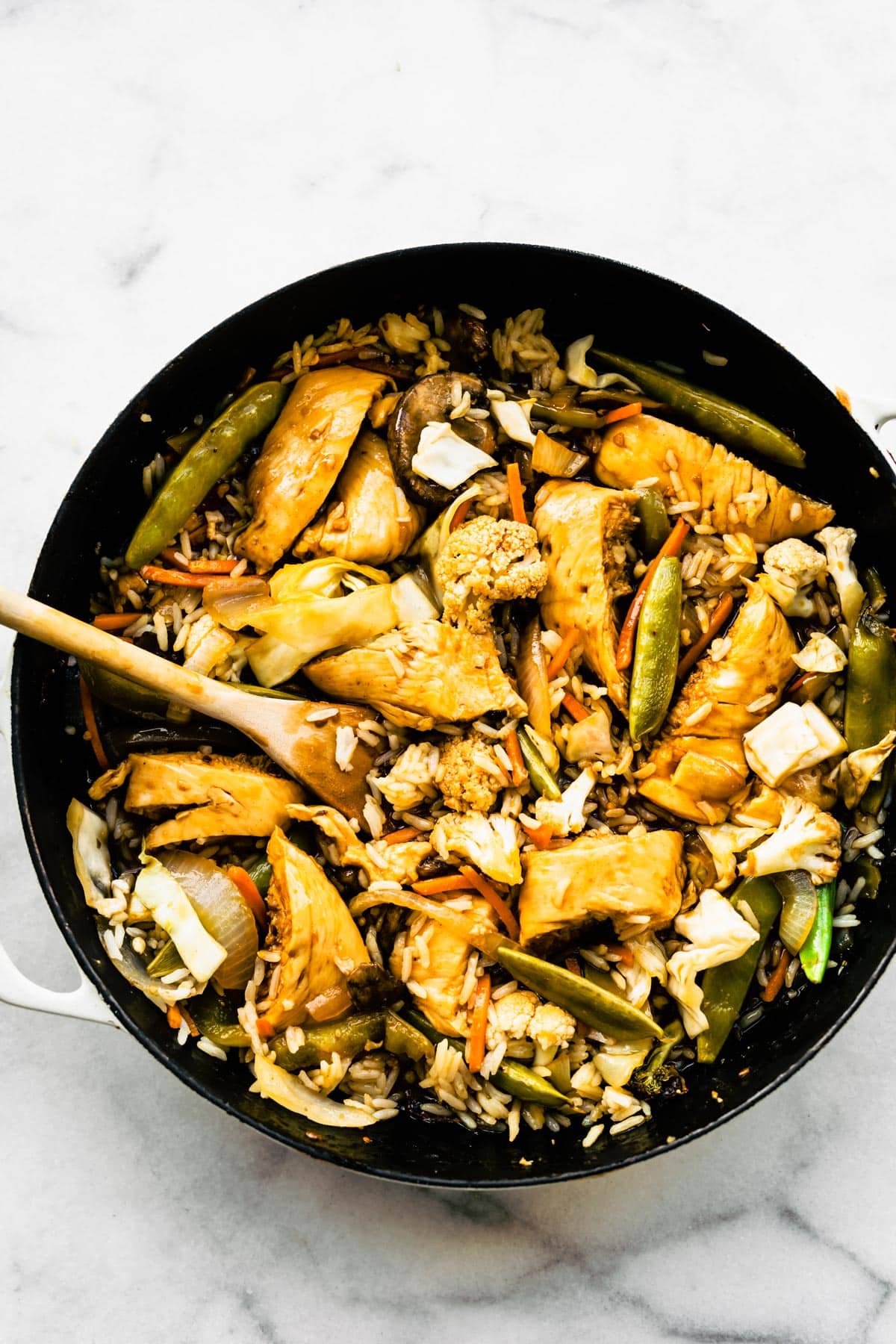 A wooden spoon stirring diced chicken breast and cooked Asian veggies in a pan.