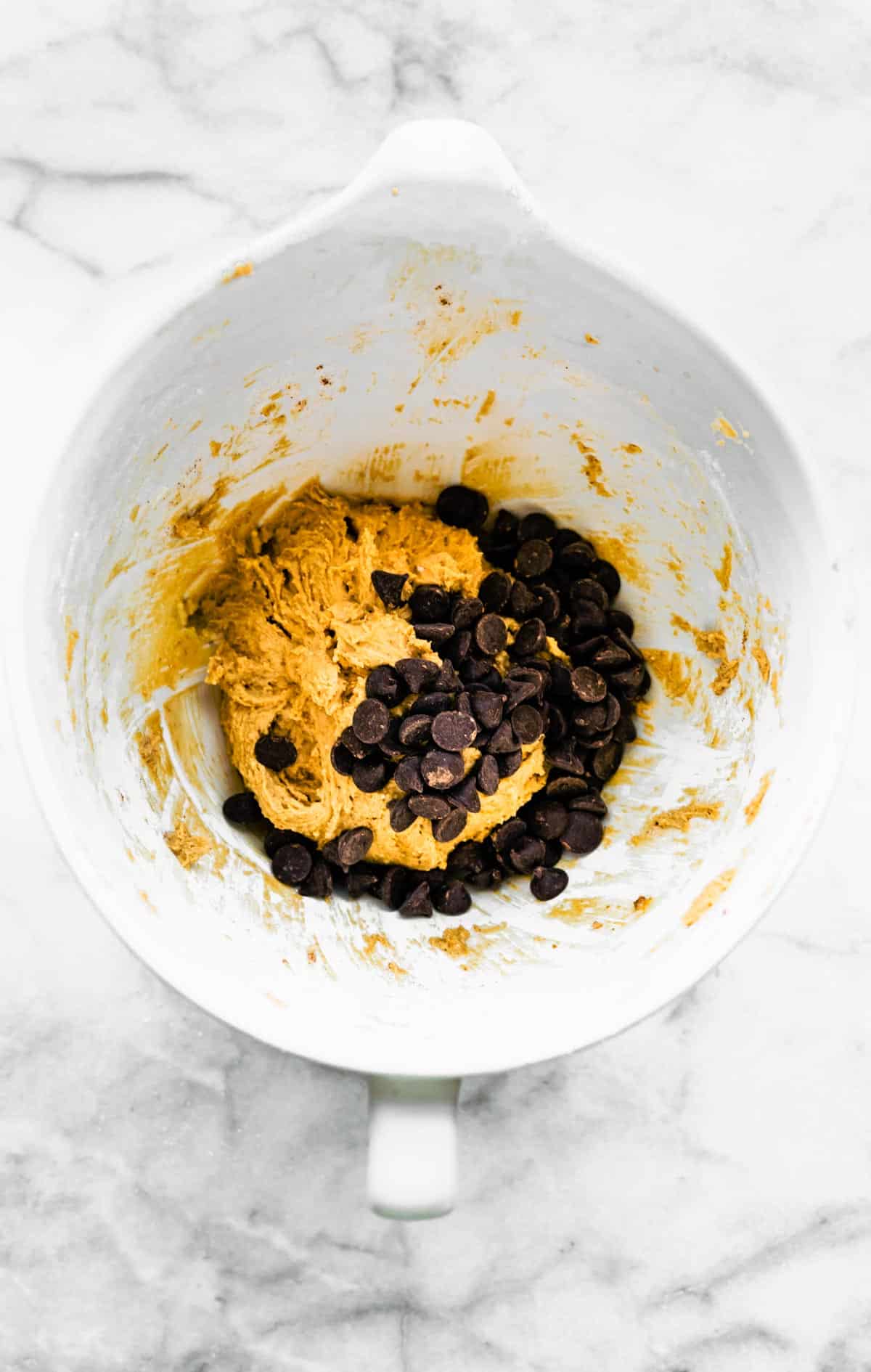 A white bowl with cookie dough and chocolate chips on a marble countertop.