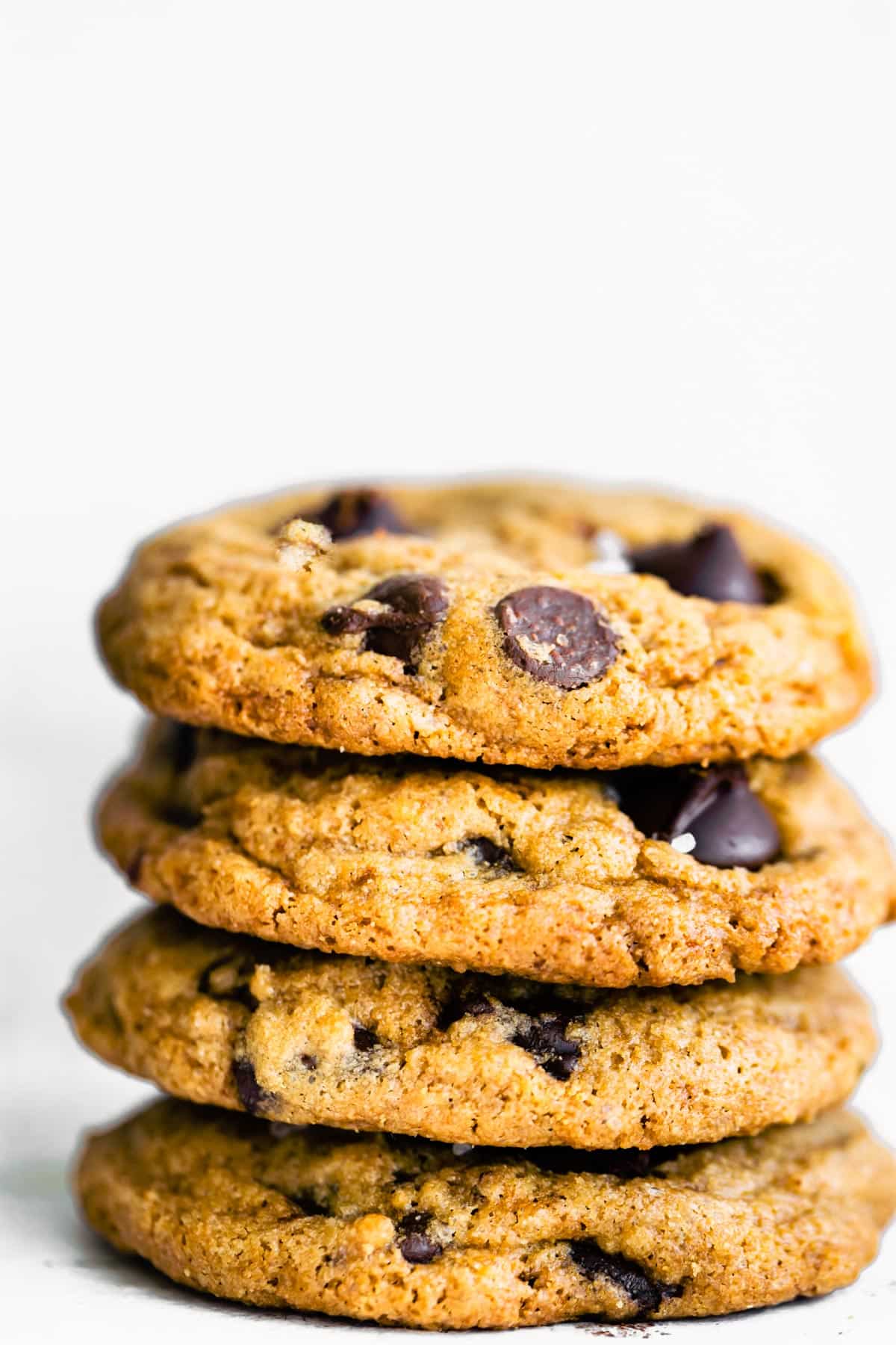 A stack of four gluten free chocolate chip cookies on a white background.
