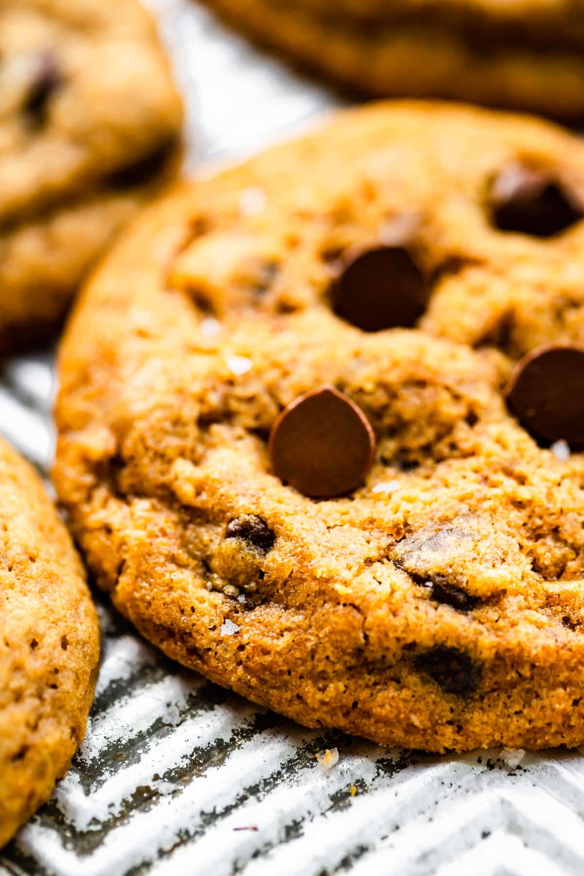 A close up of a gluten free chocolate chip cookie on a metal baking sheet.