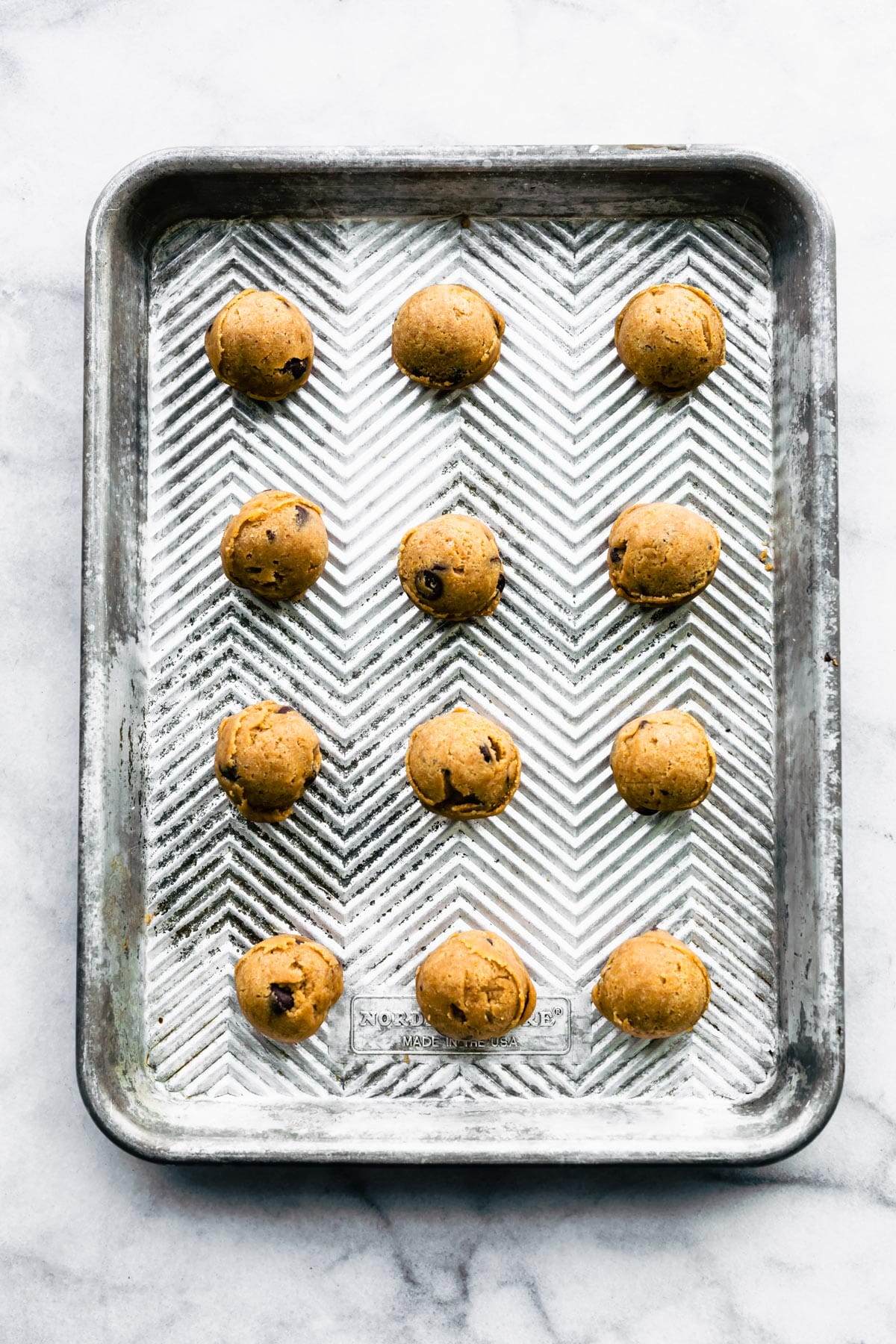 Twelve unbaked gluten free chocolate chip cookie dough balls on a baking sheet.