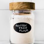 A jar of homemade gluten free flour blend with a wooden lid and black label.
