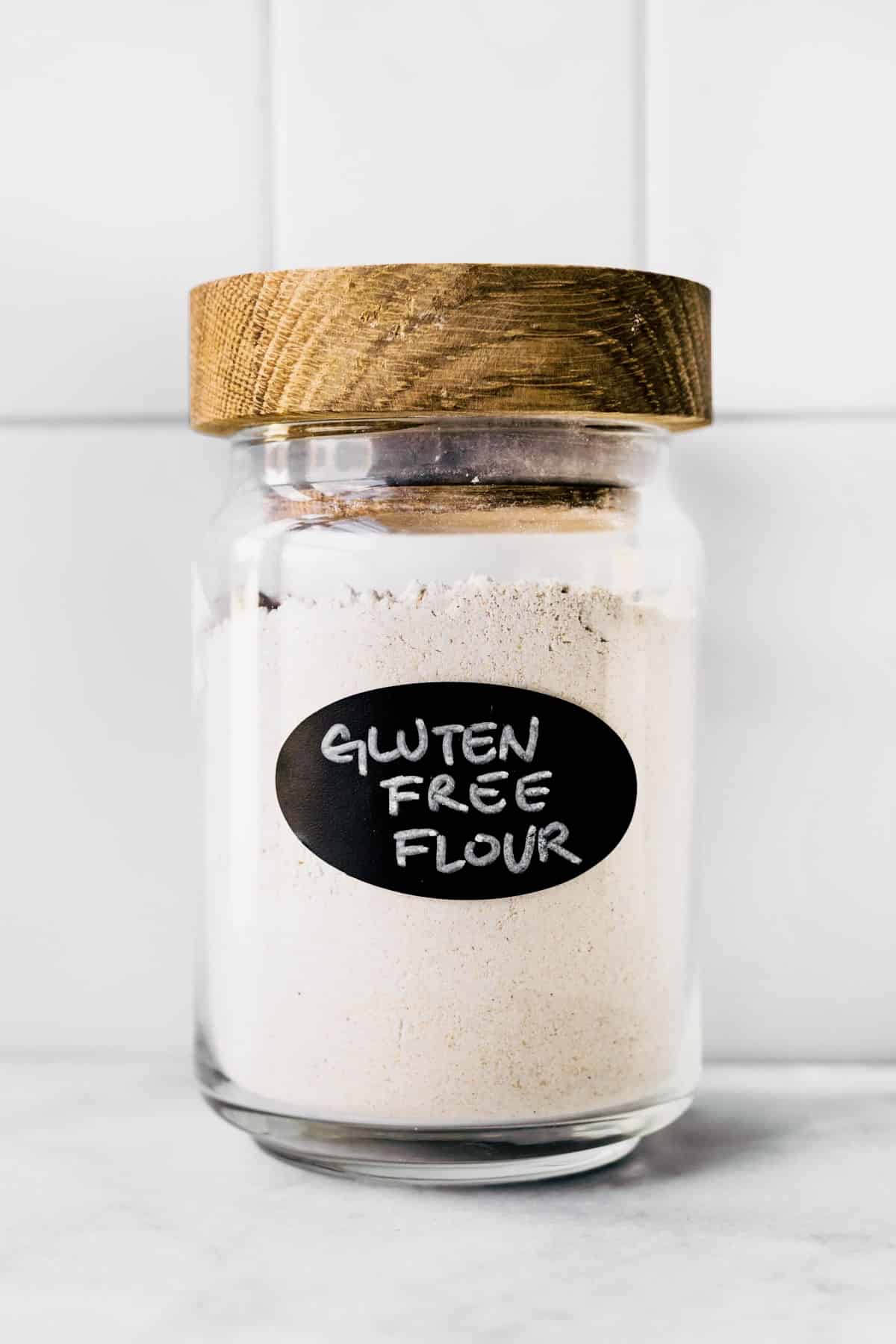 A jar of homemade gluten free flour blend with a wooden lid and black label.