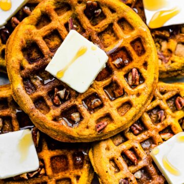 Overhead photo of pumpkin waffles on top of each other with butter, syrup and pecans.