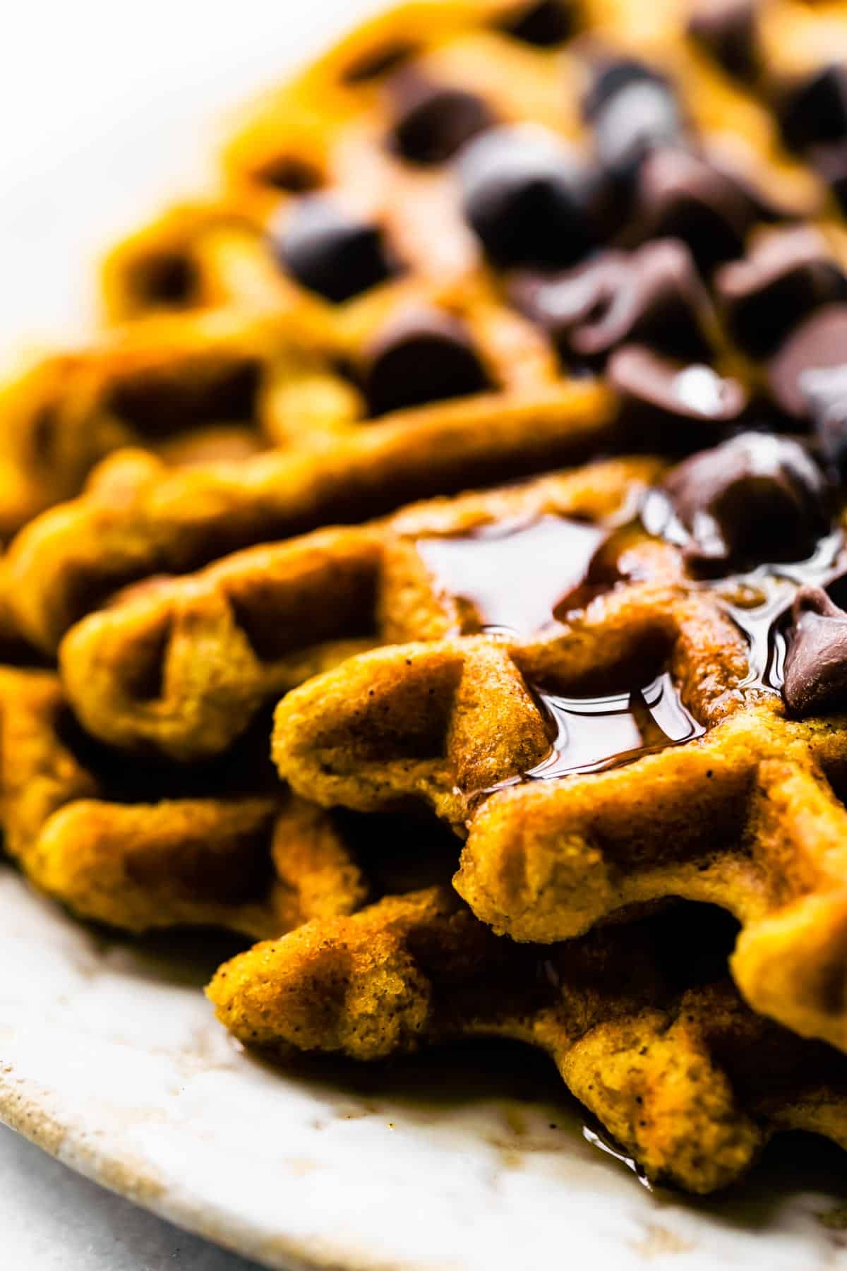 Up close photo of stacked gluten free pumpkin waffles topped with chocolate chips and syrup.