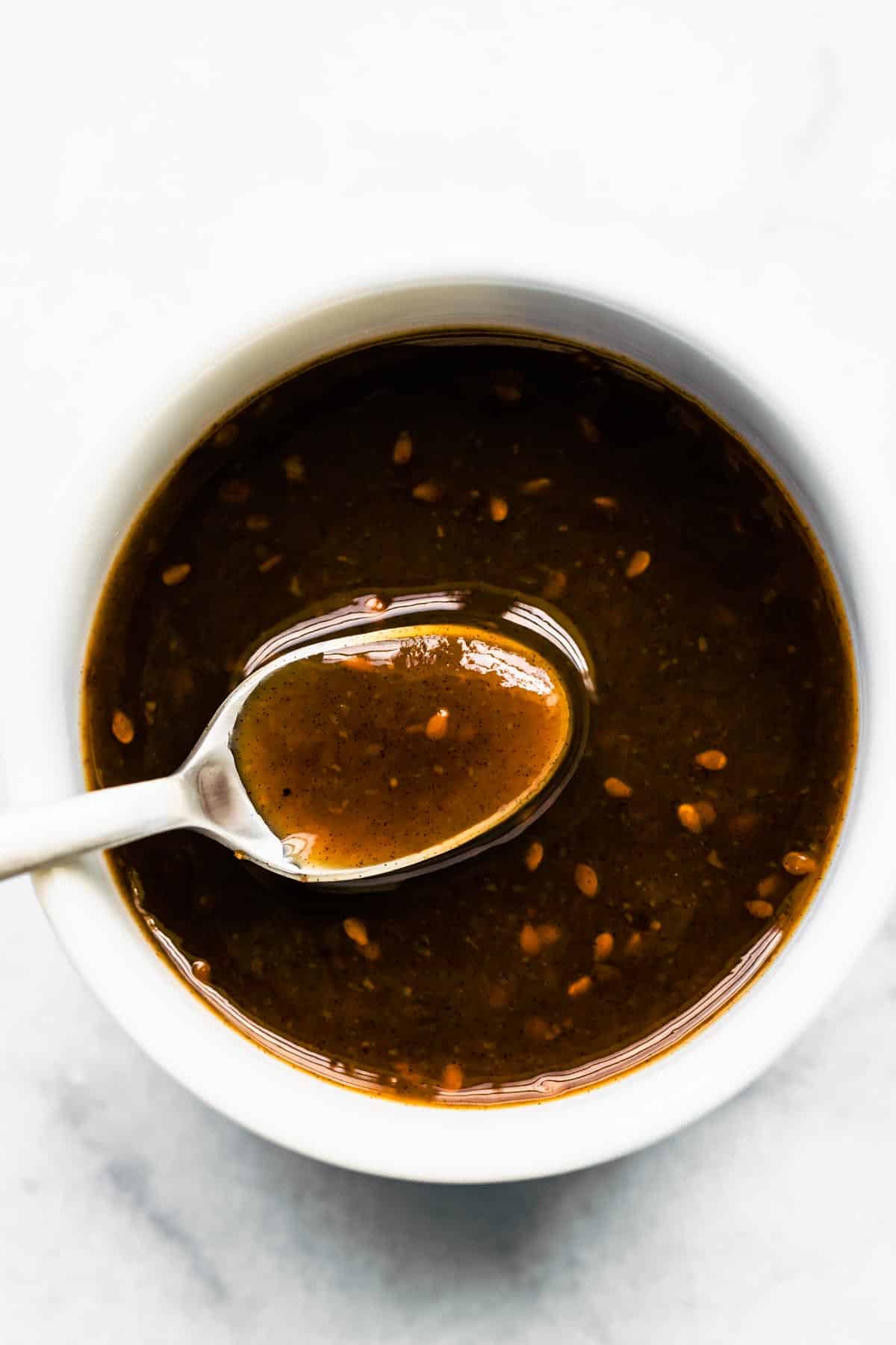 An overhead photo of a spoonful of gluten free teriyaki sauce over a white bowl.
