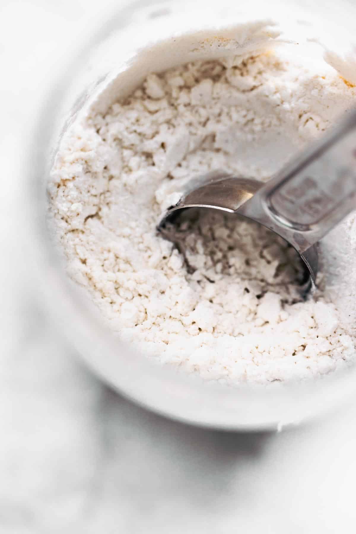 A measuring spoon dipped into a jar of gluten free flour blend.