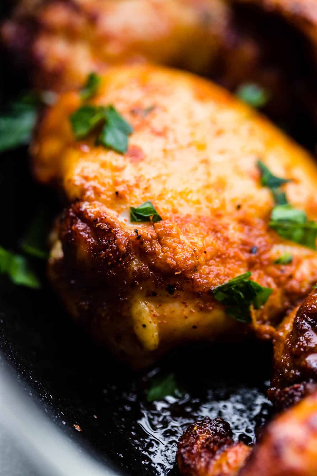 Close up photo of a baked paprika chicken thigh sprinkled with chopped parsley.