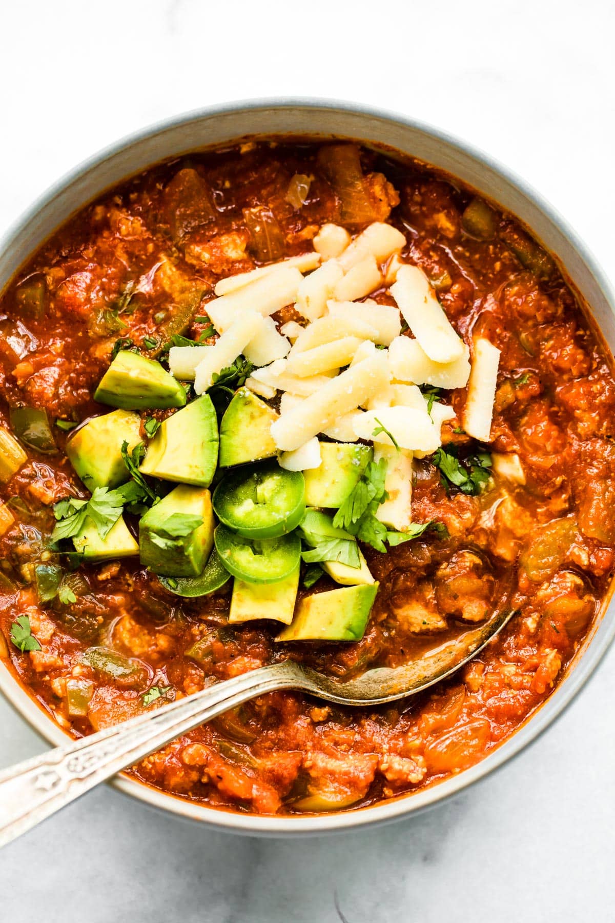 Overhead photo of a bowl of no bean chili topped with cheese, avocado and jalapenos.