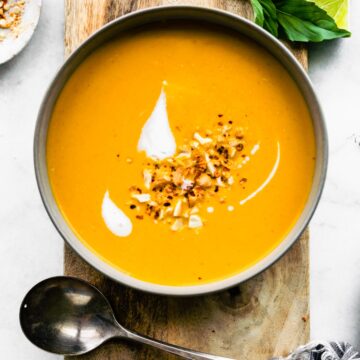 Overhead photo of Thai curried carrot ginger soup on a wooden board with a spoon.