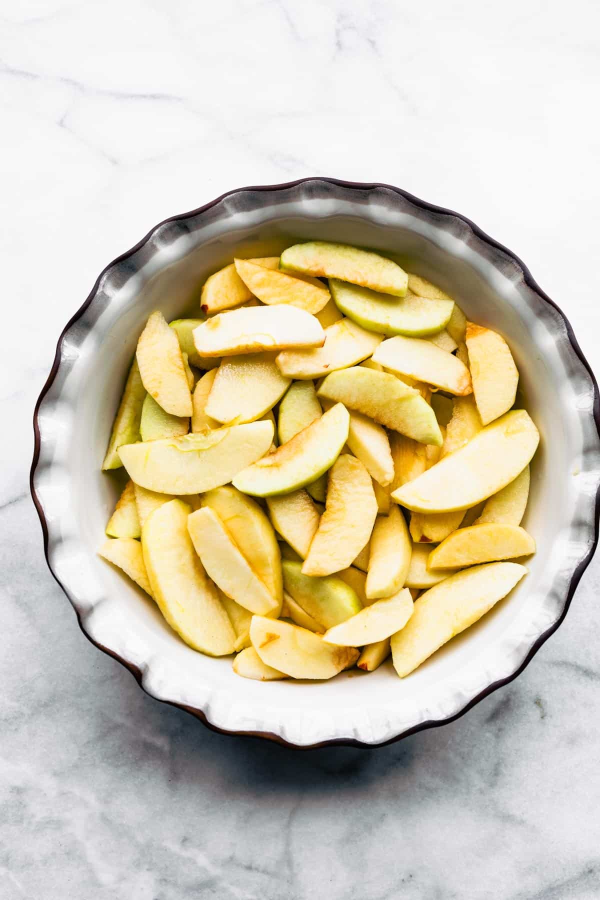 Overhead photo of peeled and slices apples in a white ceramic pie pan.