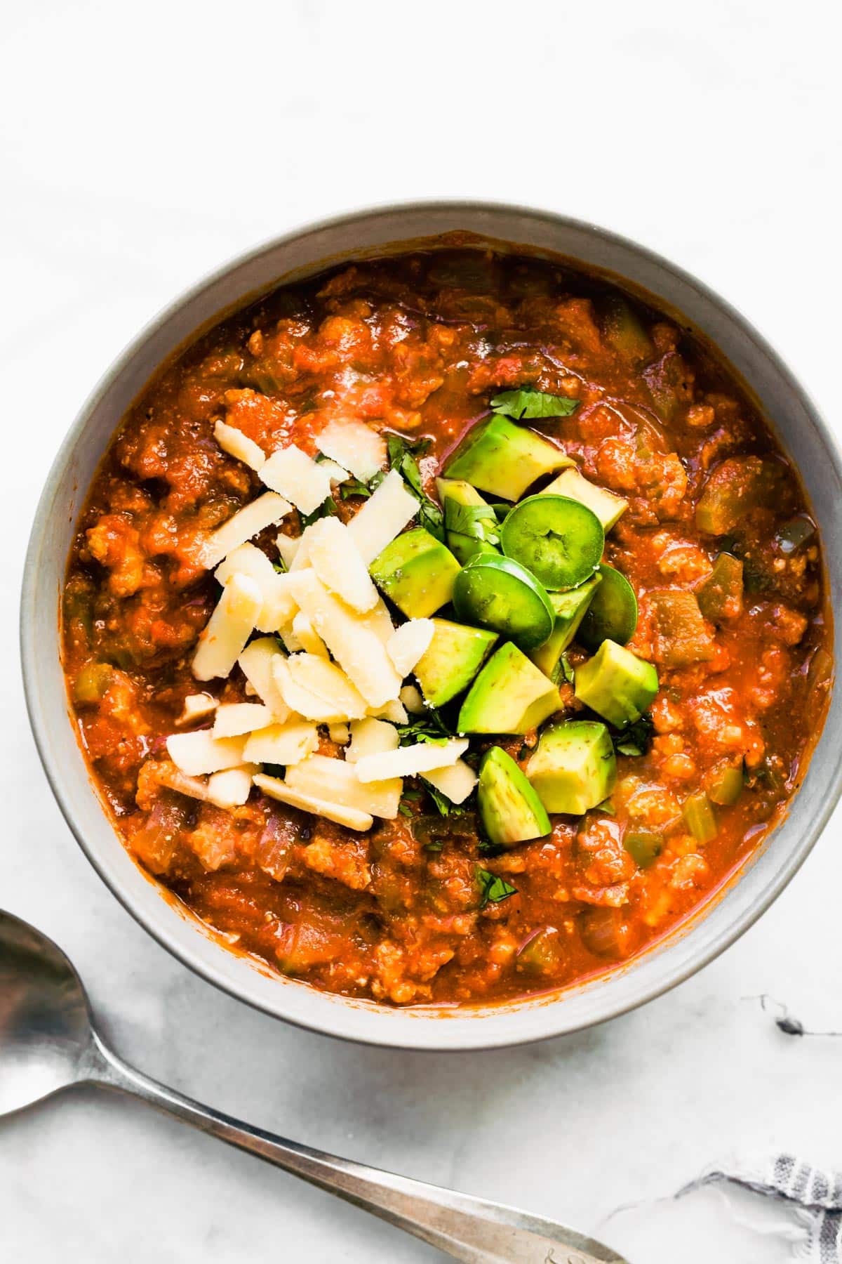 Overhead photo of no bean chili topped with shredded cheese, jalapenos and avocado.