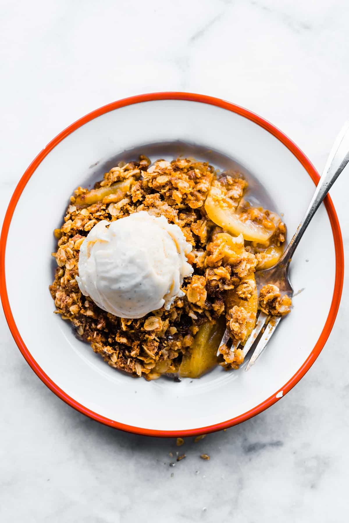 Gluten free apple crisp in a bowl with vanilla ice cream and a fork.