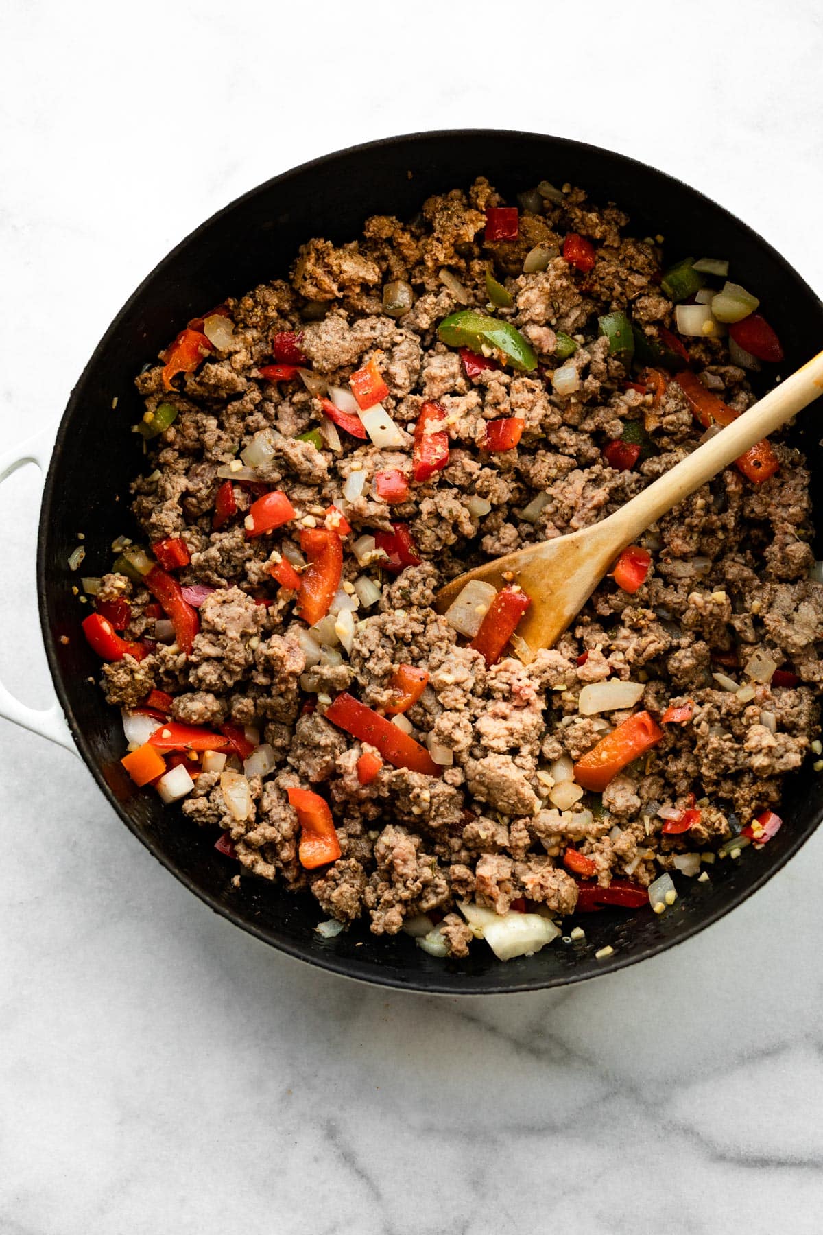 A wooden spoon mixing browned ground beef with diced bell peppers and onions.