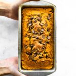 Two woman's hands holding a loaf of gluten free pumpkin bread in a metal pan.