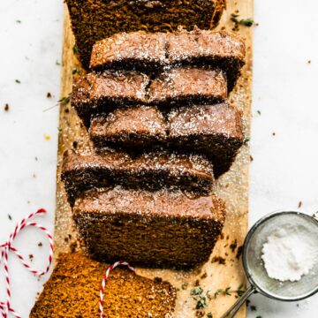 Overhead photo of sliced gingerbread loaf on a wooden cutting board sprinkled with powdered sugar.