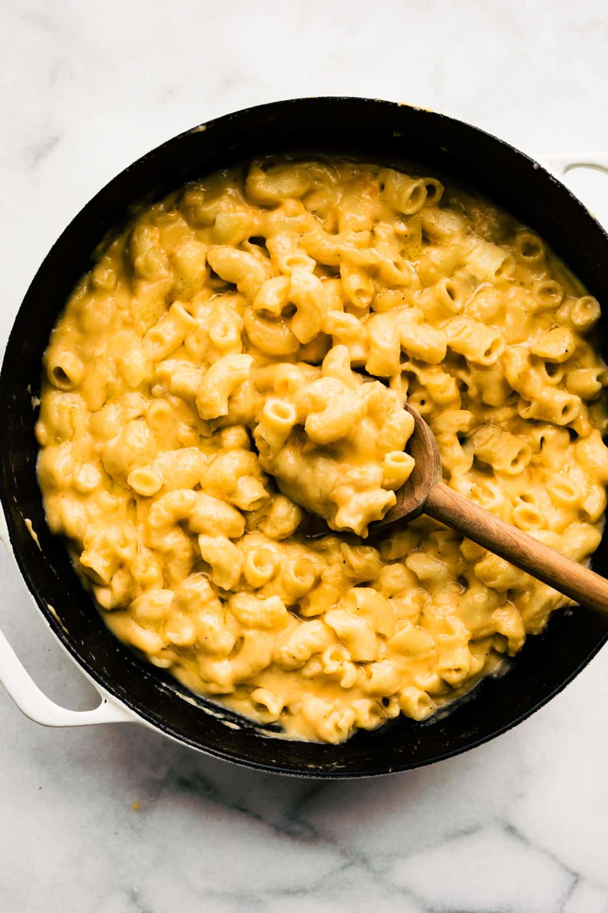 A wooden spoon in a pan of gluten free mac and cheese.