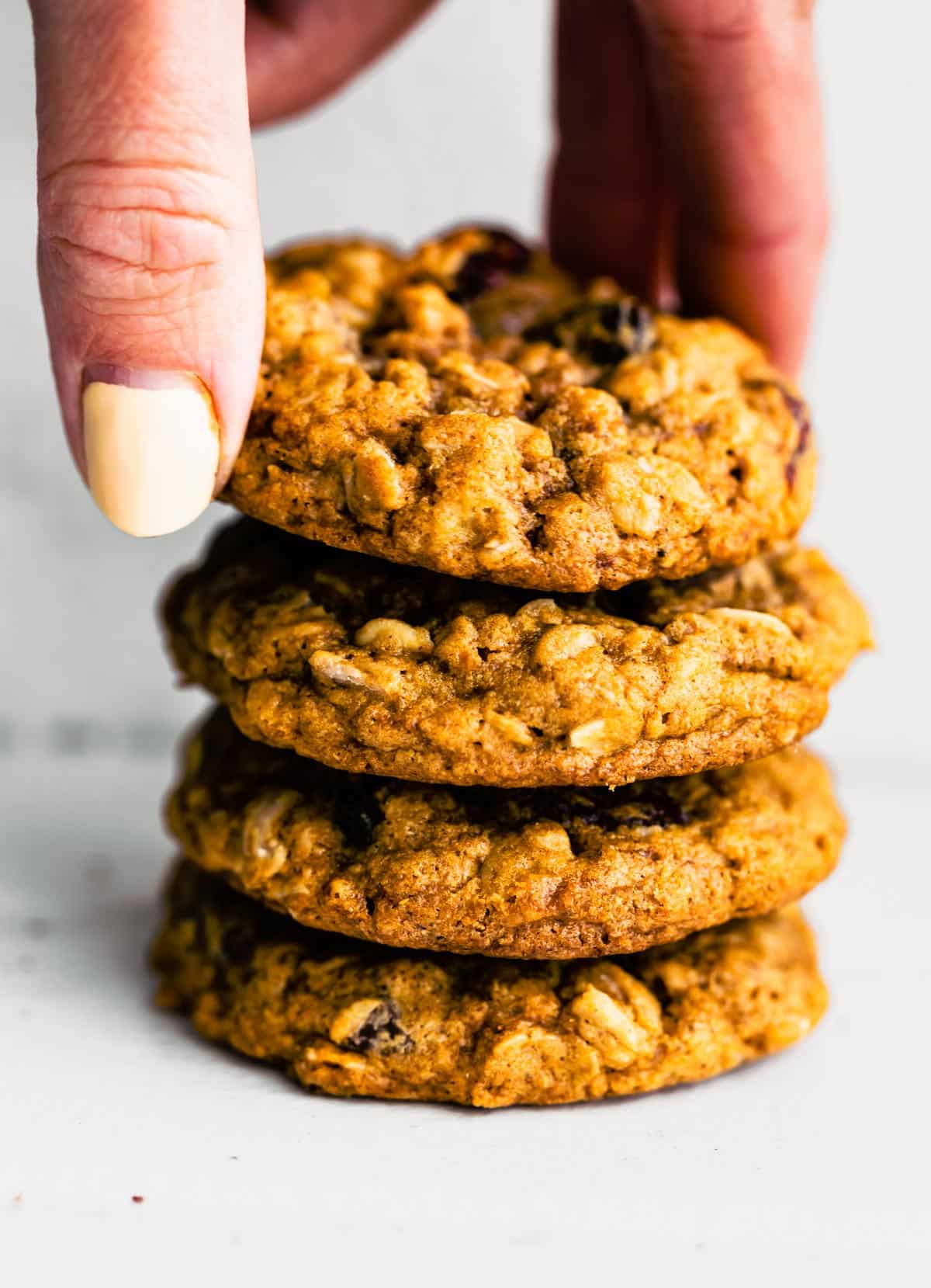 A woman's hand grabbing a gluten free oatmeal cookie from a stack of four cookies.