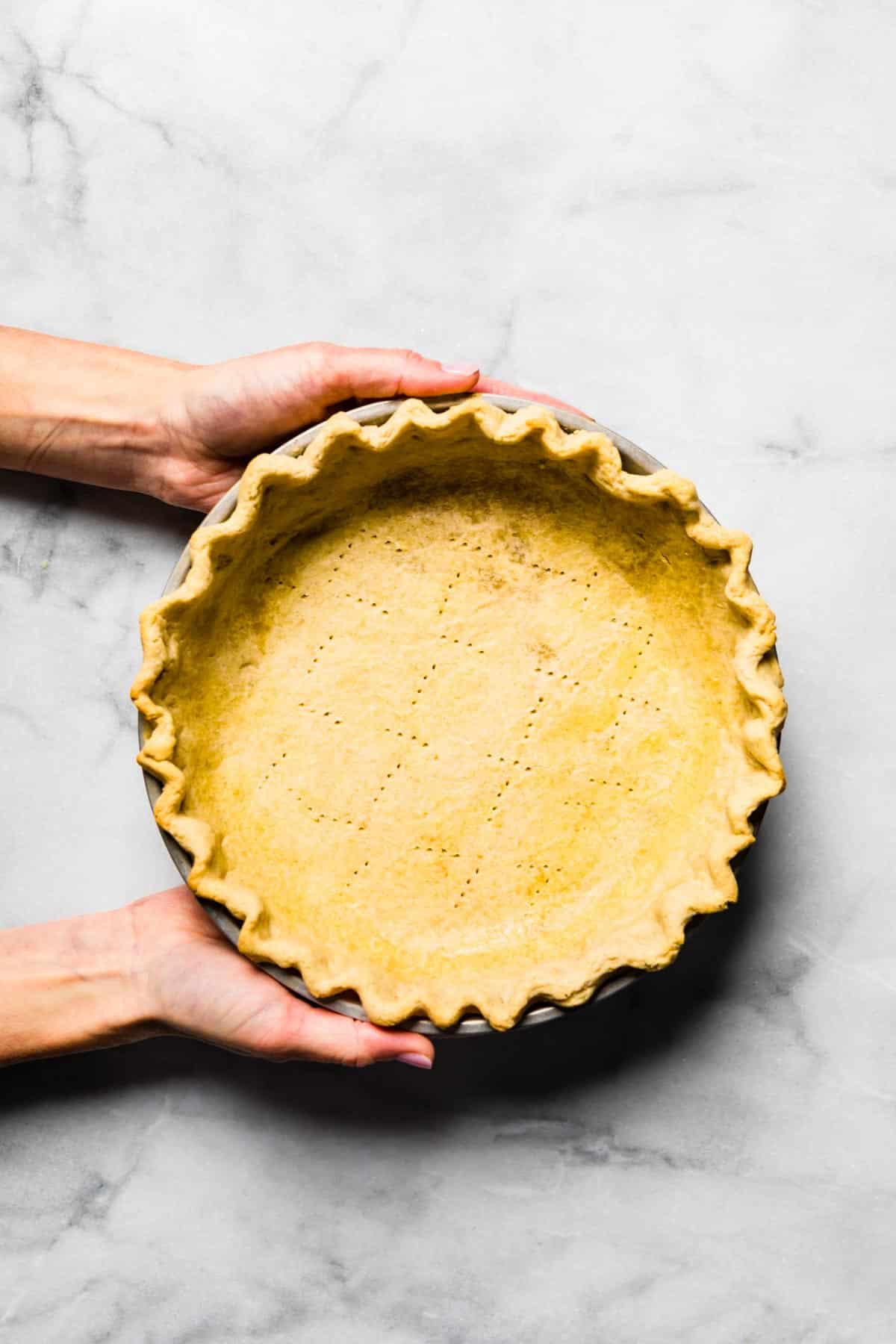 A woman's hands holding a docked gluten free pie crust that is par baked.