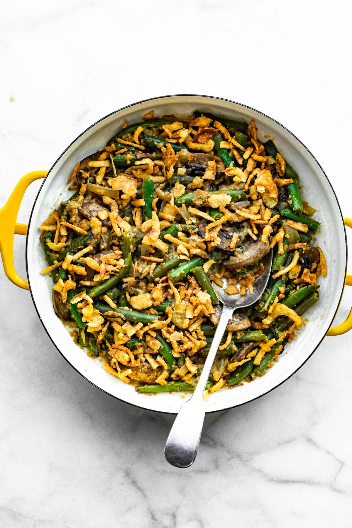 A serving spoon in a pan of vegan green bean casserole topped with fried onions.