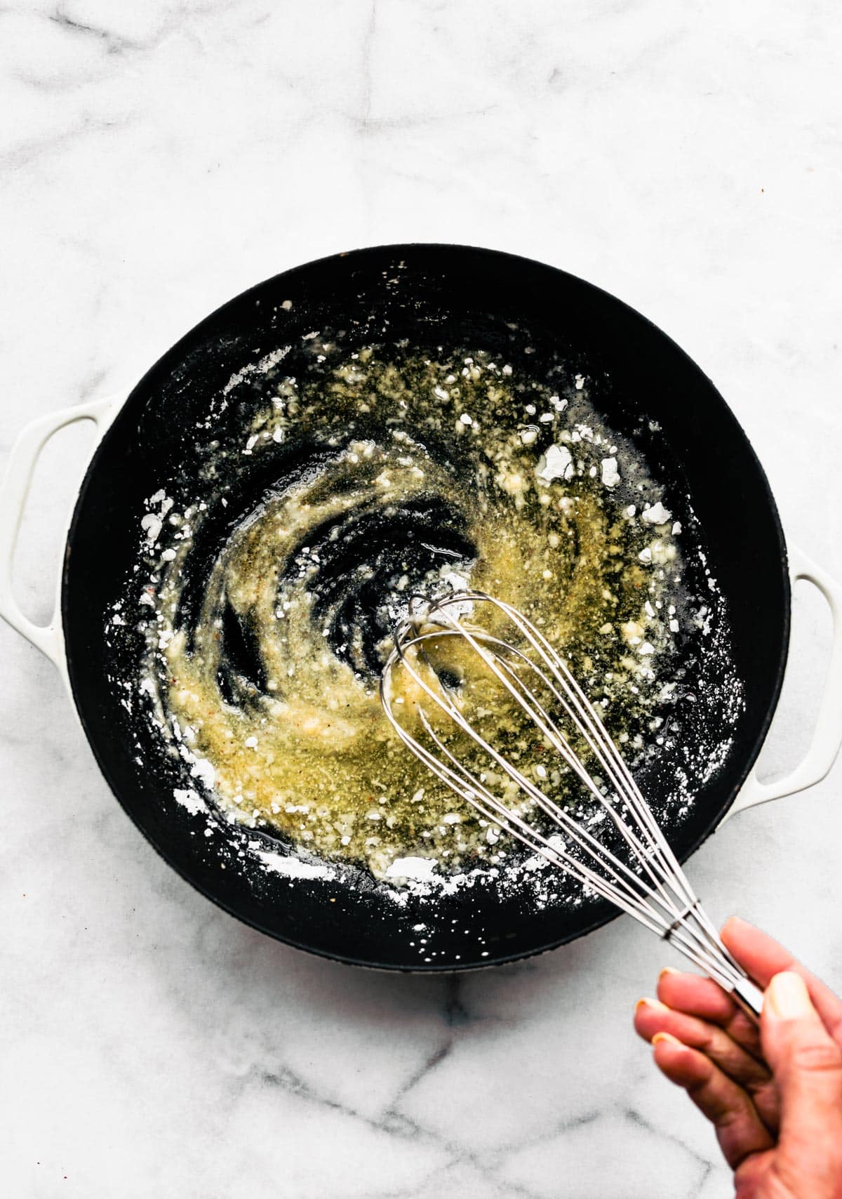 A woman whisking gluten free flour into melted butter in a pan.