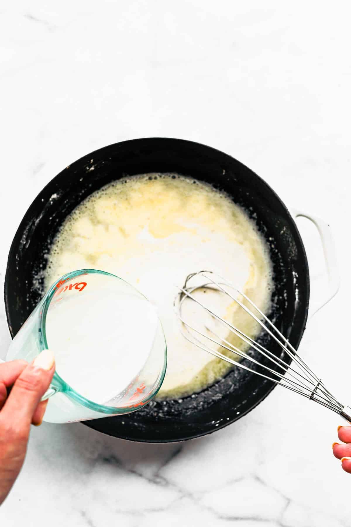 A woman's hand whisking coconut milk into a pan of melted butter and flour.