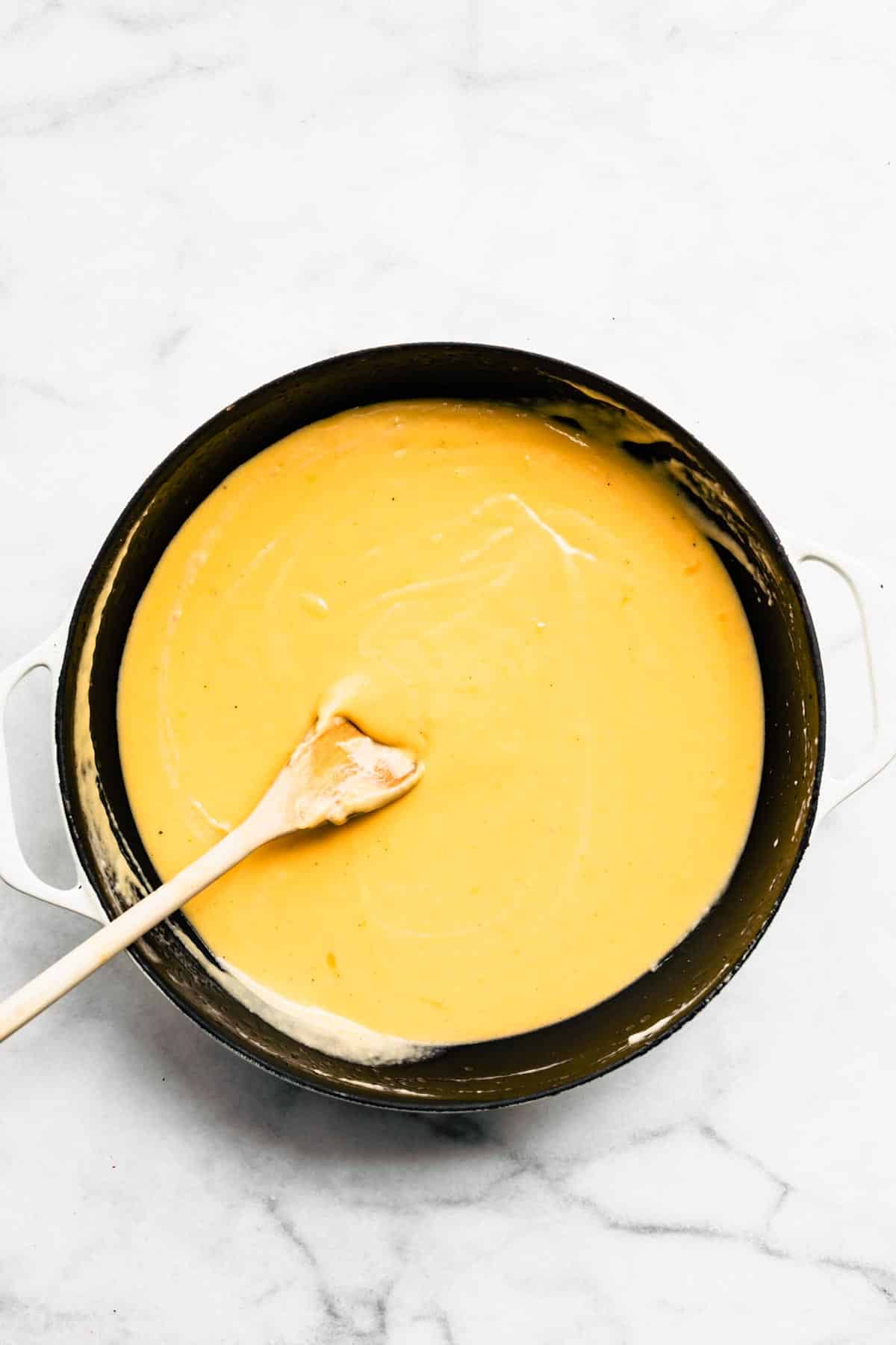 Overhead photo of a wooden spoon in a pan of vegan cheese sauce.