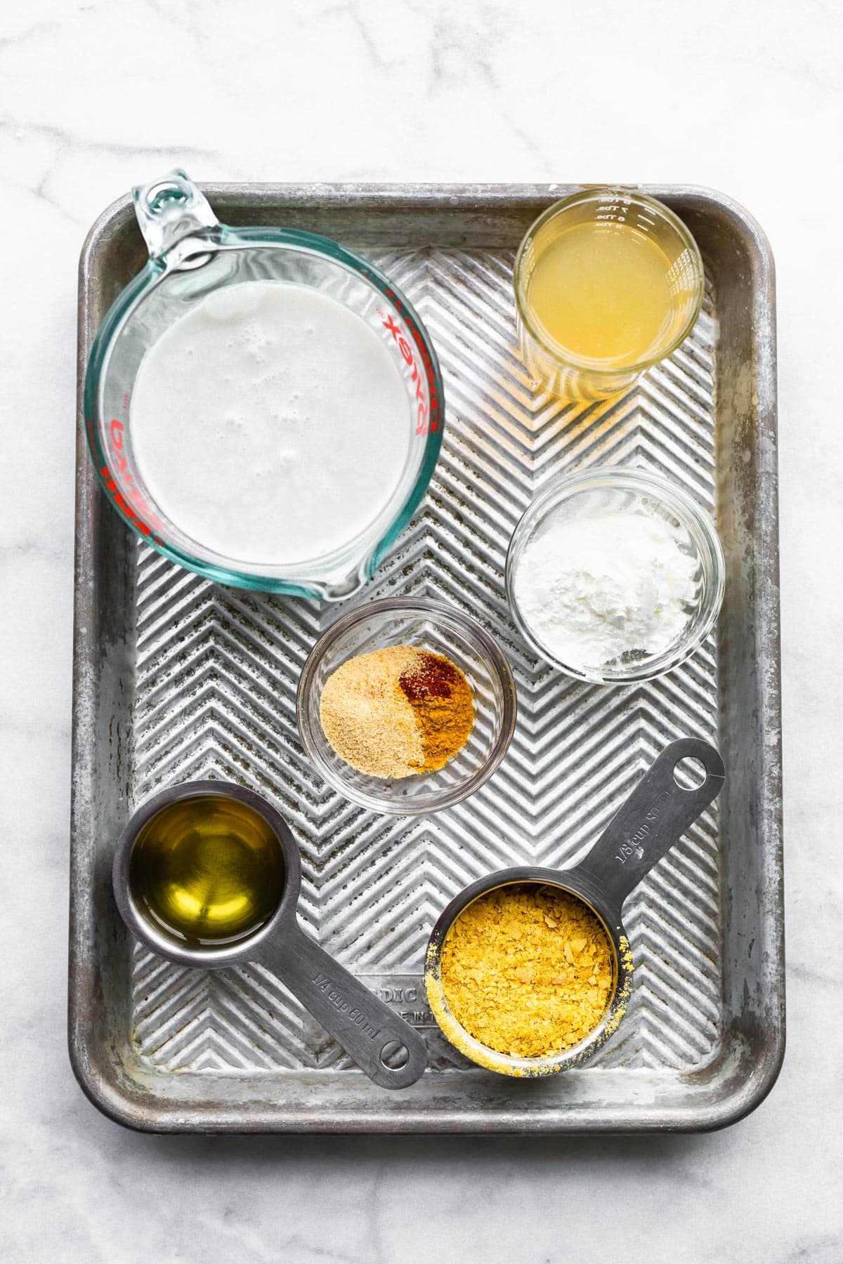 Bowls of ingredients to make vegan cheese sauce on a metal baking sheet.