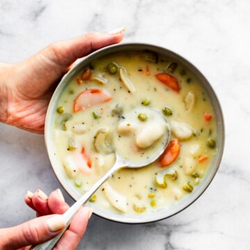 A woman's hand holding a bowl of creamy chicken and gnocchi soup.