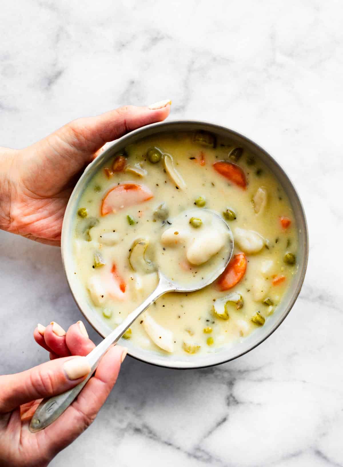 A woman's hand holding a bowl of creamy chicken and gnocchi soup.