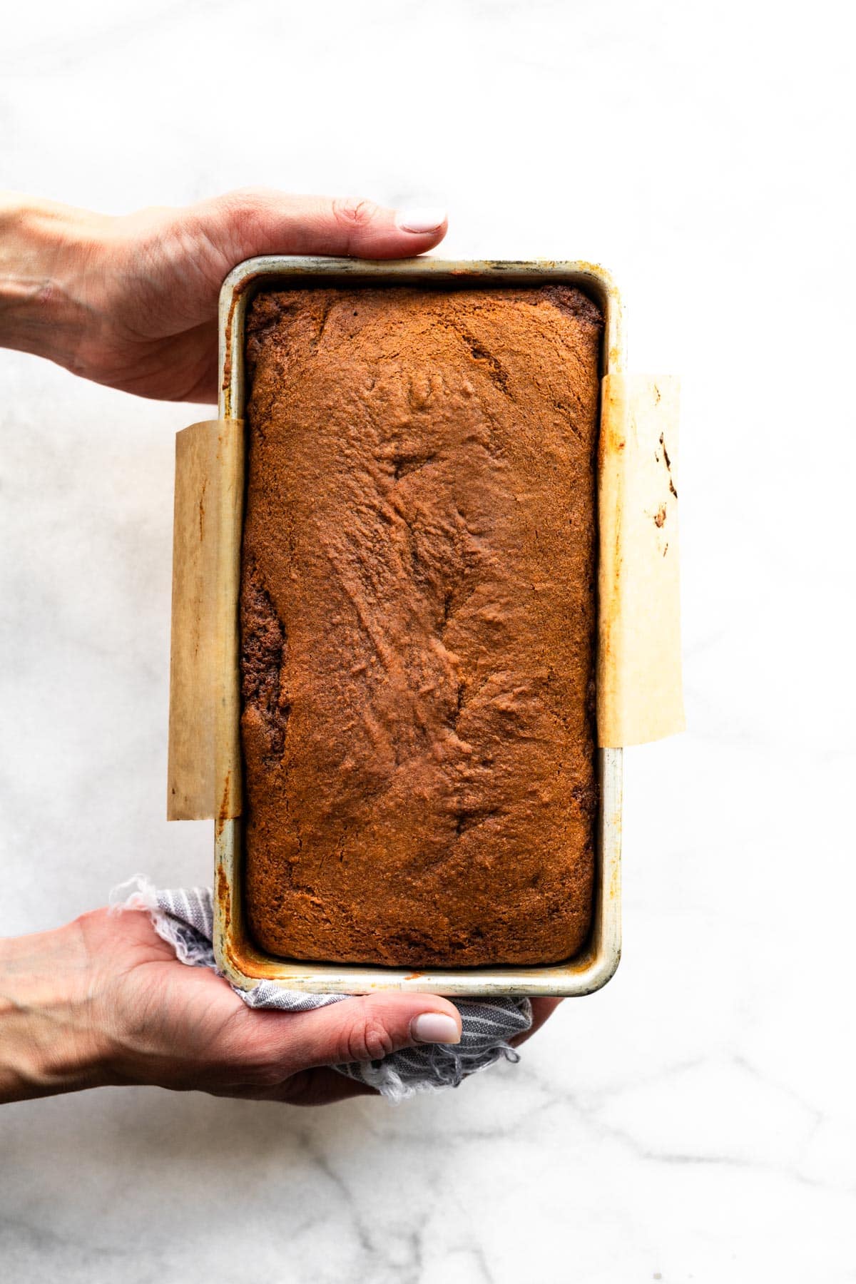 A woman's hands holding a loaf of gluten free gingerbread in a metal pan.