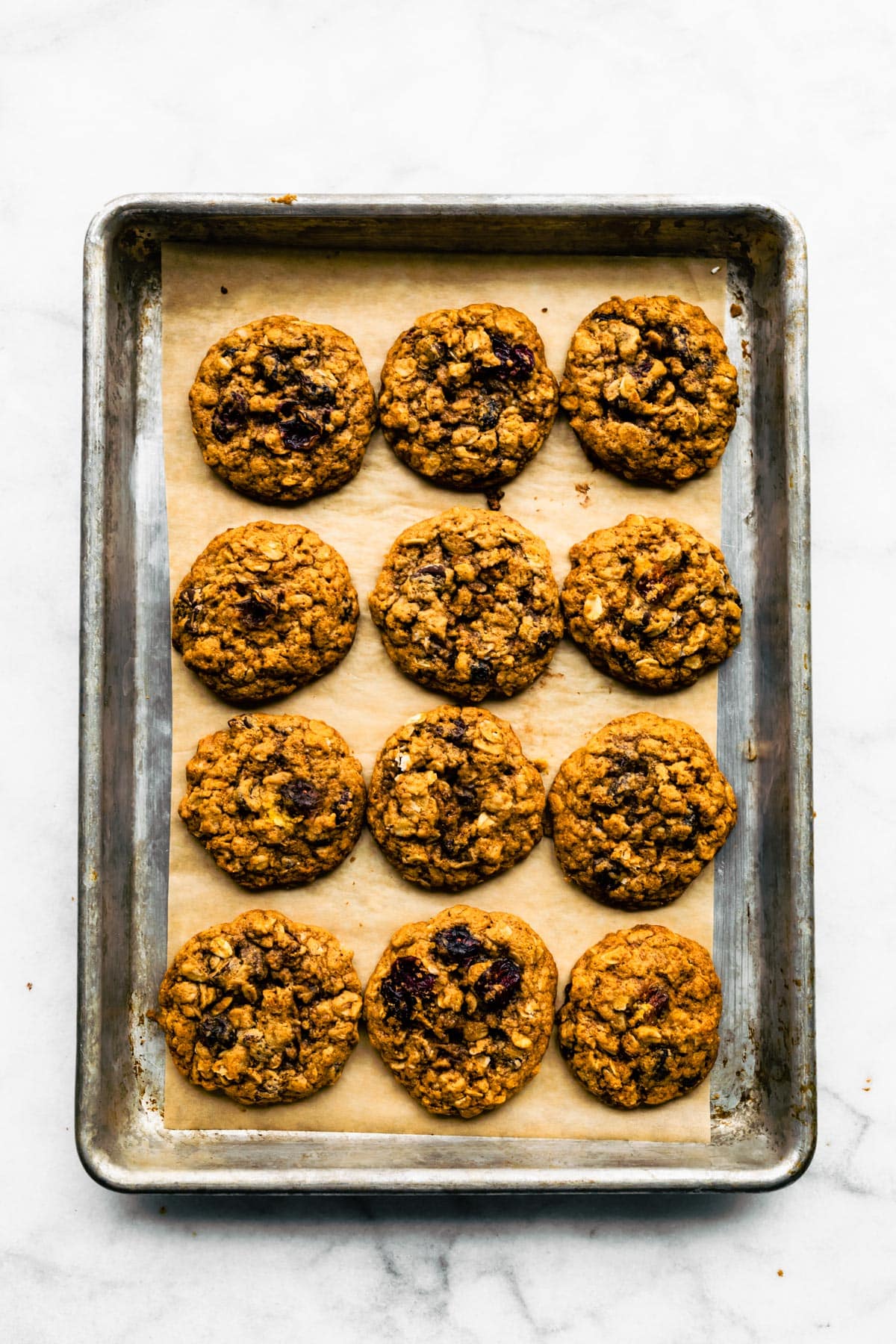 Overhead photo of twelve baked cranberry oatmeal cookies on a metal baking sheet.