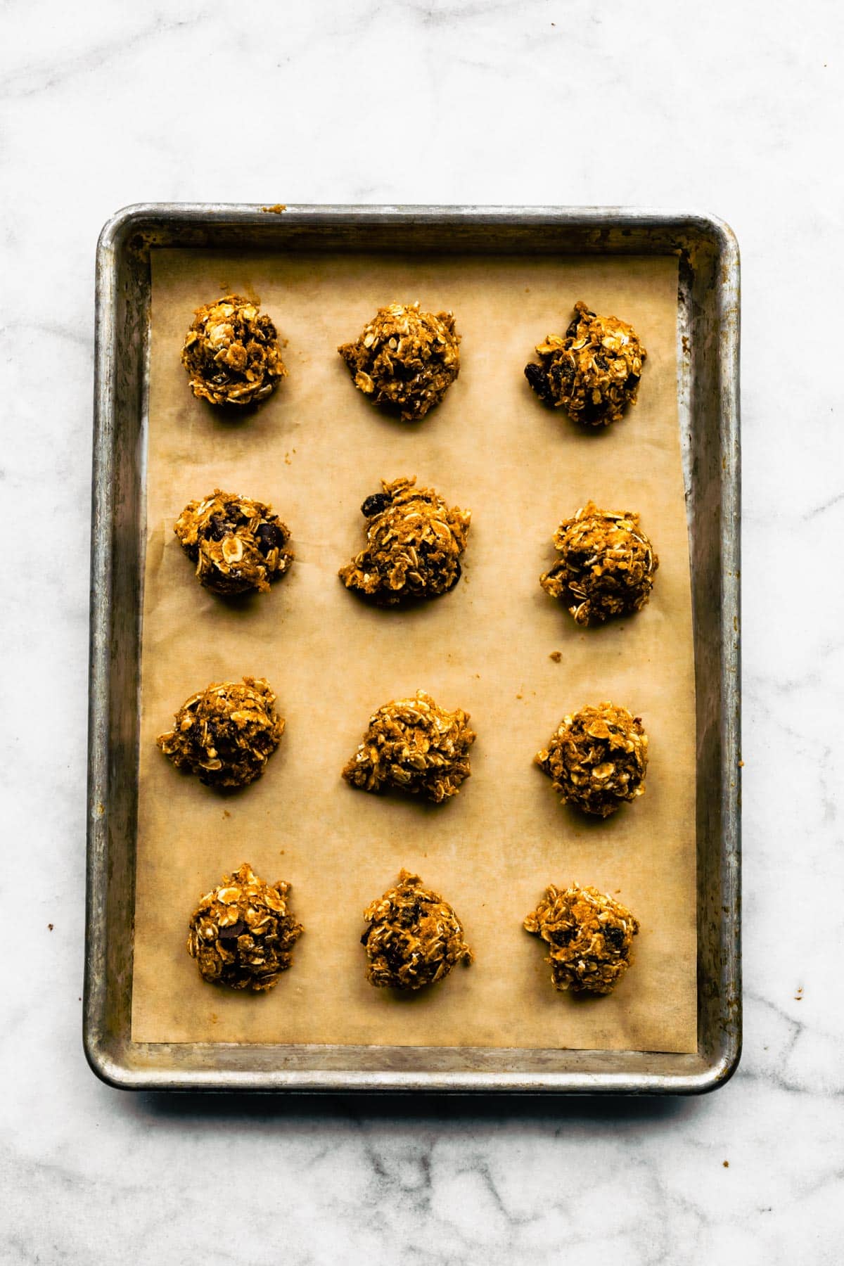 Twelve pieces of oatmeal cookie dough on parchment paper on a baking sheet.