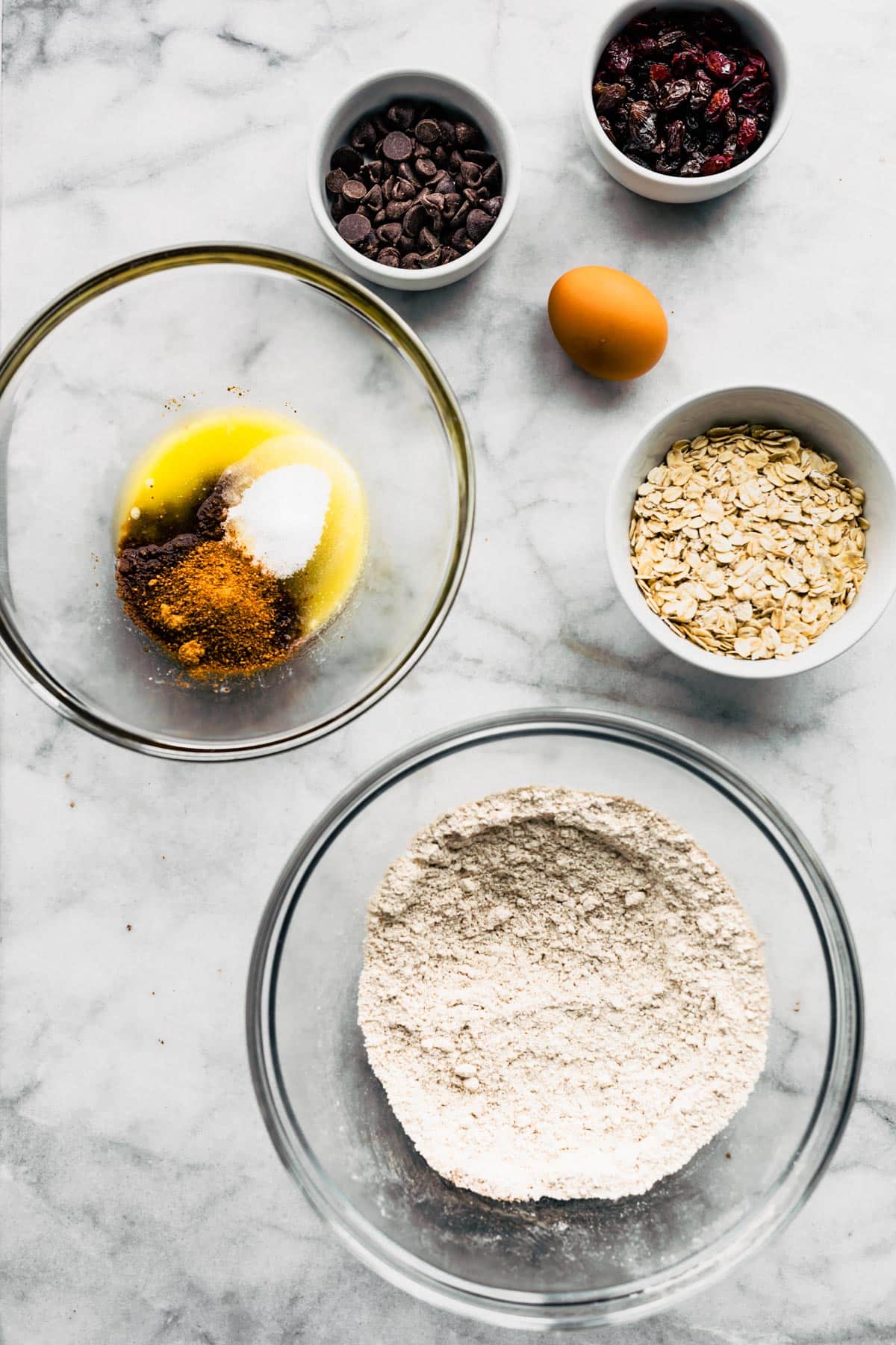 Bowls of ingredients for gluten free oatmeal cookies on a white marble countertop.