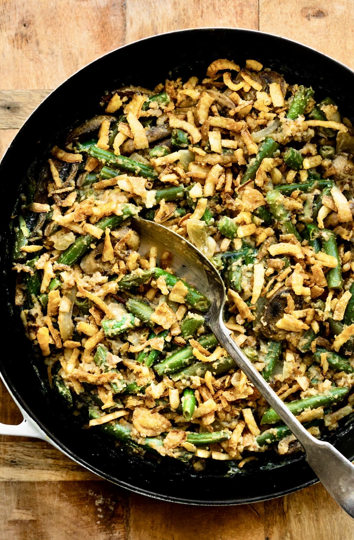 Overhead close up photo of a spoon in a pan of vegan green bean casserole.