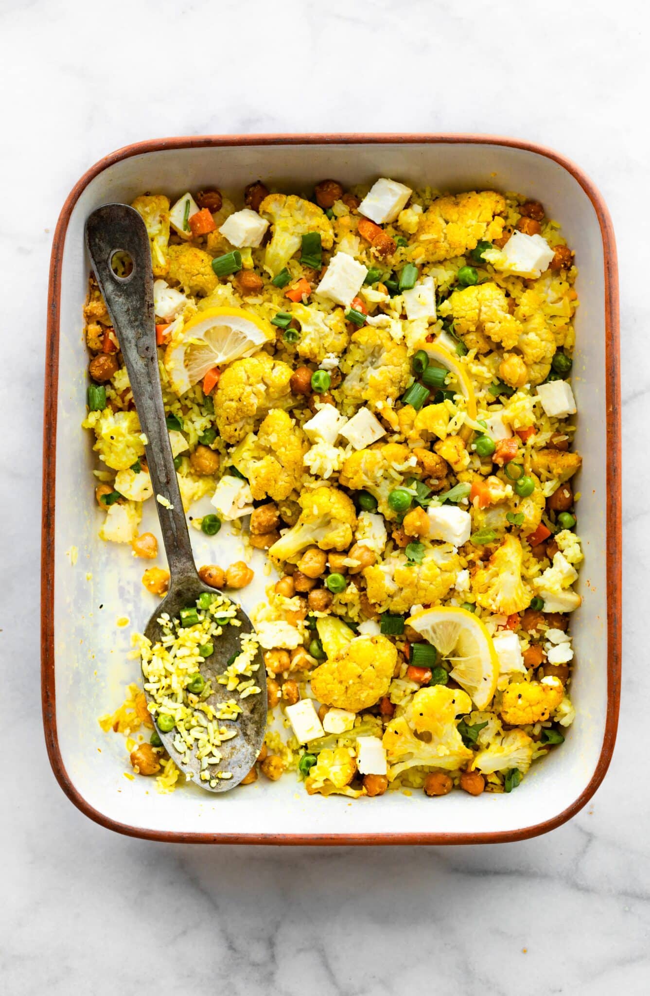 Overhead photo of curried cauliflower chickpea bake with a serving removed with a spoon.