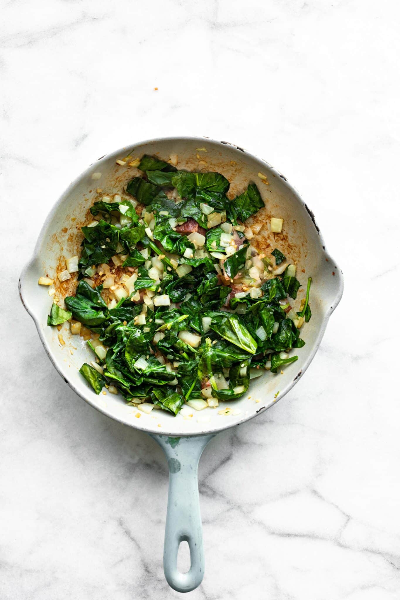 Overhead photo of sauteed onion, garlic and spinach in a sauté pan.