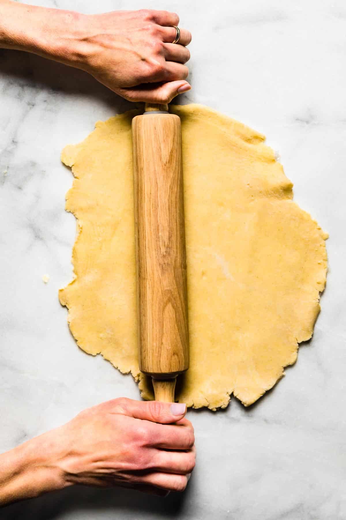 A woman's hands using a wooden rolling pin to roll out a pie crust.