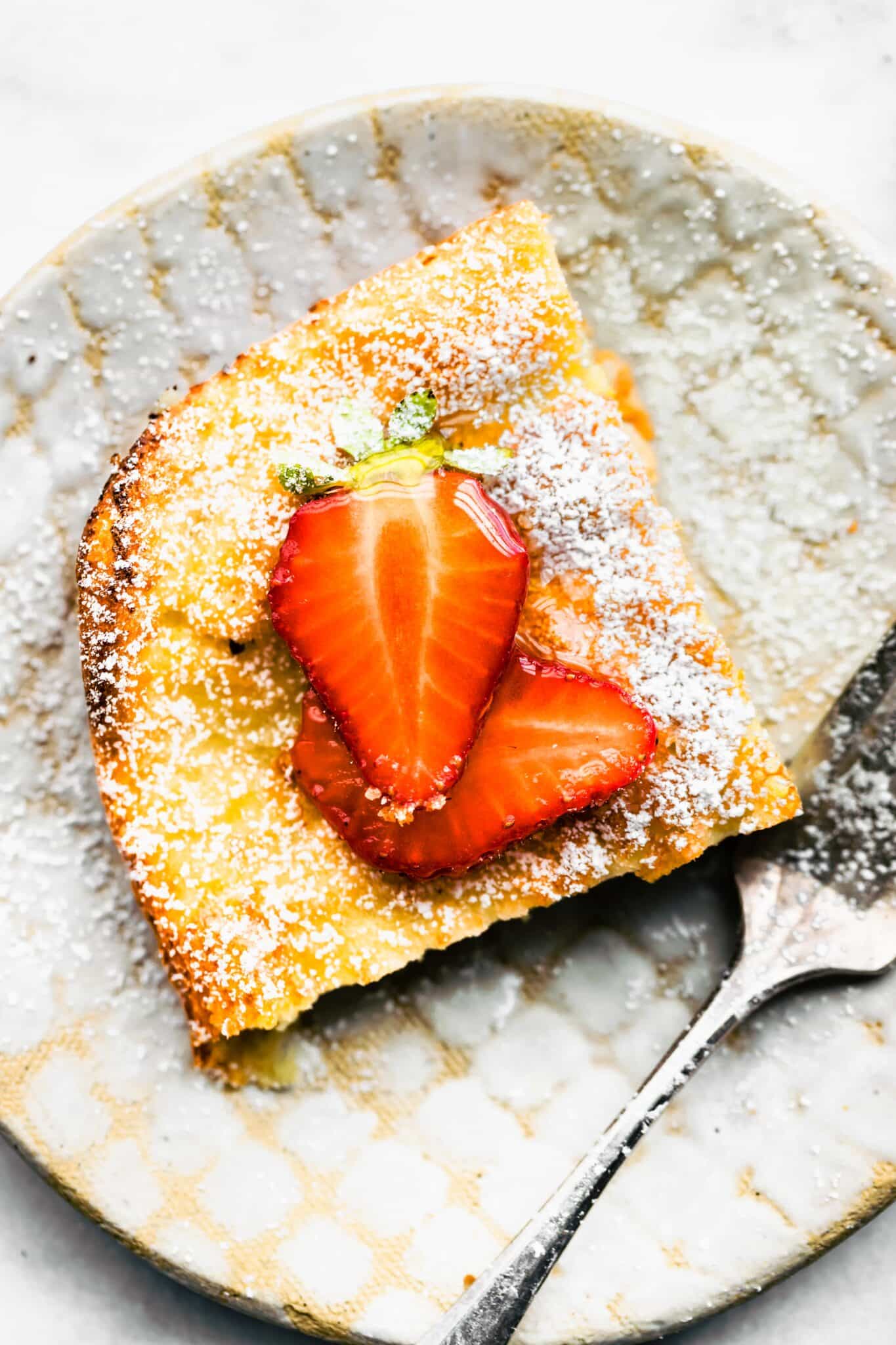 Overhead photo of a slice of Swedish Pancakes topped with strawberries and powdered sugar.