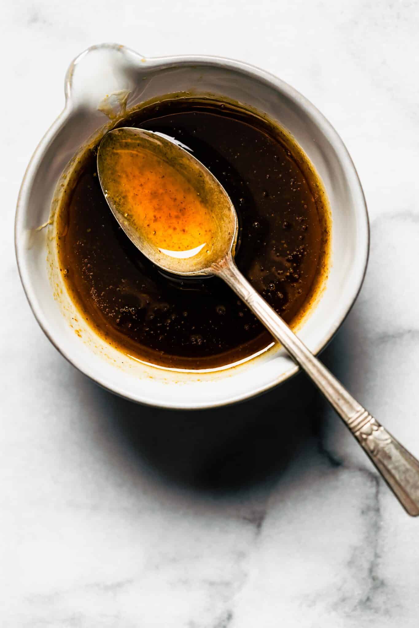 A spoon with maple bourbon glaze over a bowl of low sugar glaze.