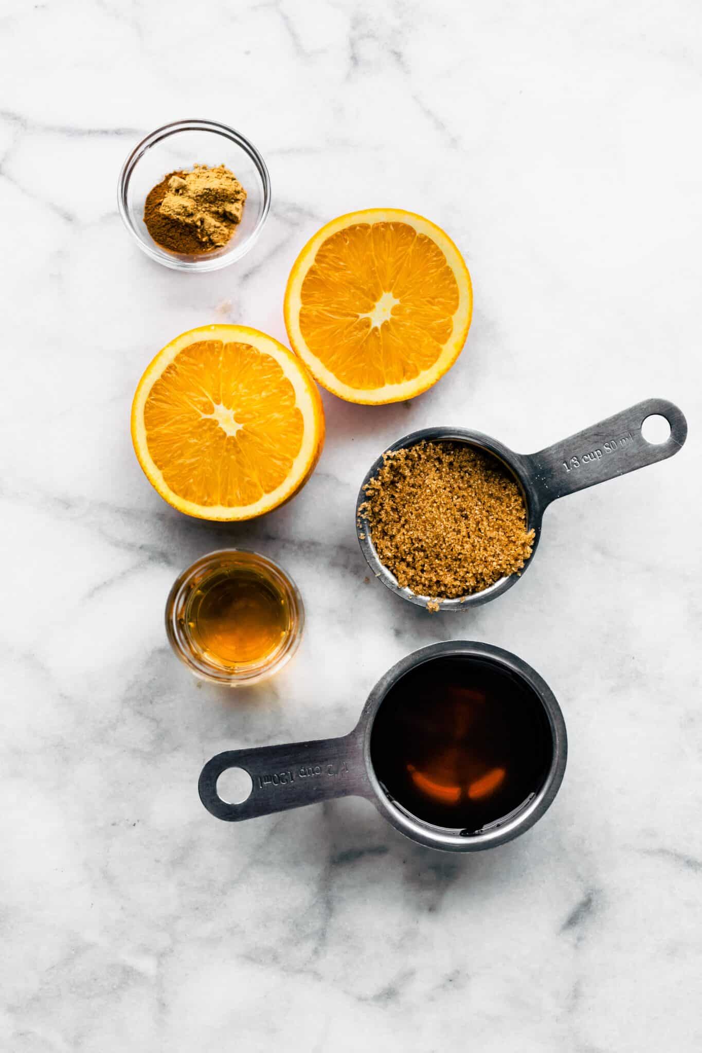 Measuring cups filled with coconut sugar and maple syrup and fresh oranges on a countertop.