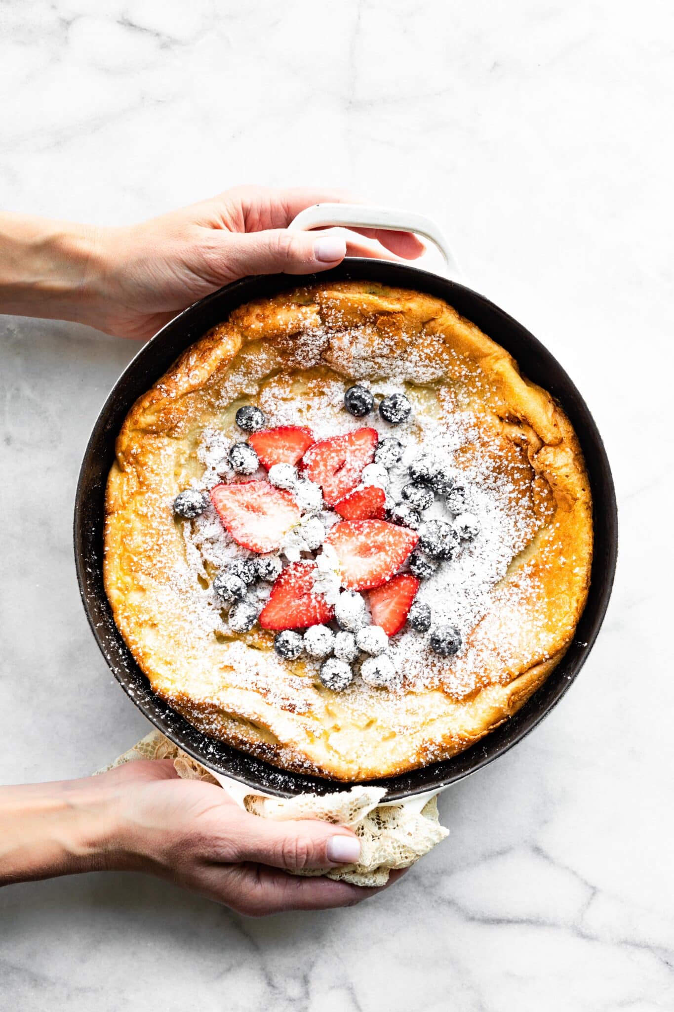 A woman's hands holding a cast iron pan of Swedish Pancakes topped with berries.